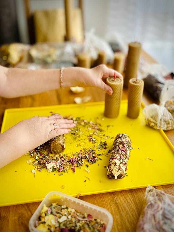 Close-up of hands crafting floral scented candles on a yellow tray.